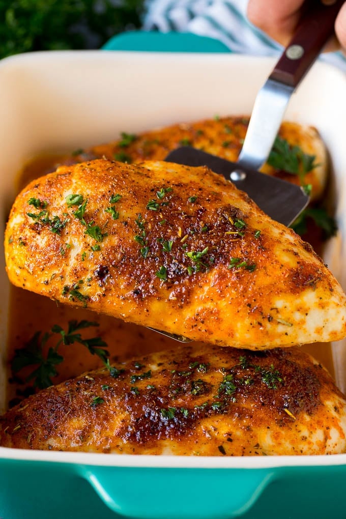 Baked Chicken Breast Recipe #chicken #dinner #edsug A spatula serving up a portion of roasted chicken breast.
