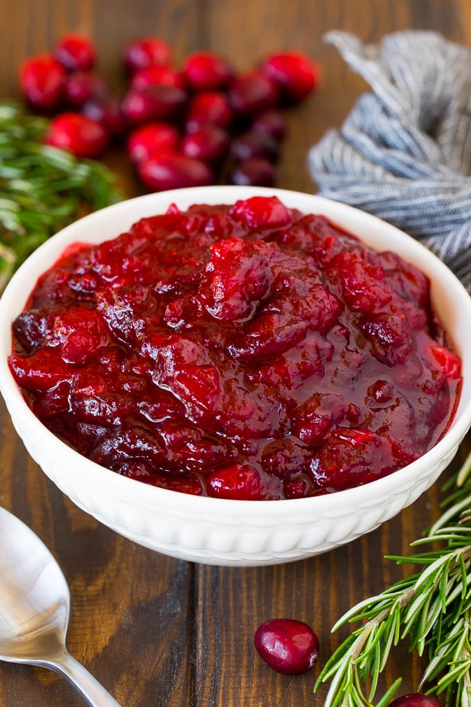 This homemade cranberry sauce is a 6 ingredient recipe that's made with fresh cranberries, sugar and a hint of spice. A bowl of homemade cranberry sauce with a serving spoon and garnishes.