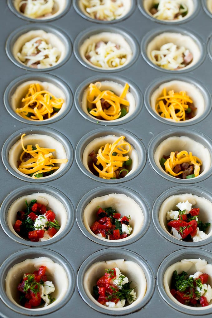 Mini Quiche Recipe #eggs #breakfast #brunch #appetizer #edsug Muffin tins filled with pie crust, vegetables, meat and shredded cheese.