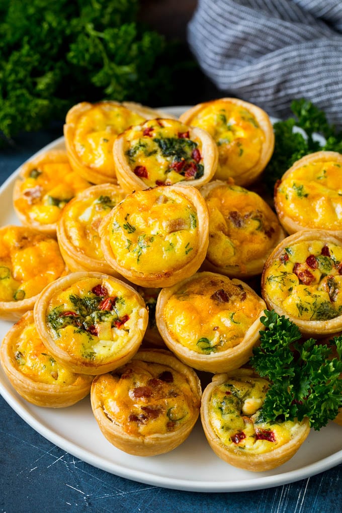 Mini Quiche Recipe #eggs #breakfast #brunch #appetizer #edsug A plate of mini quiche filled with meats, vegetables and cheeses.