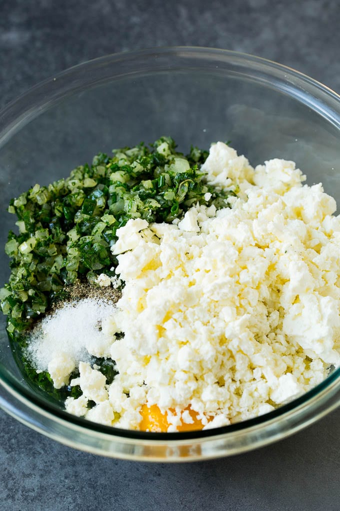 Spanakopita Recipe #appetizer #snack #spinach #cheese #edsug Spinach, onions, herbs and feta cheese in a bowl.