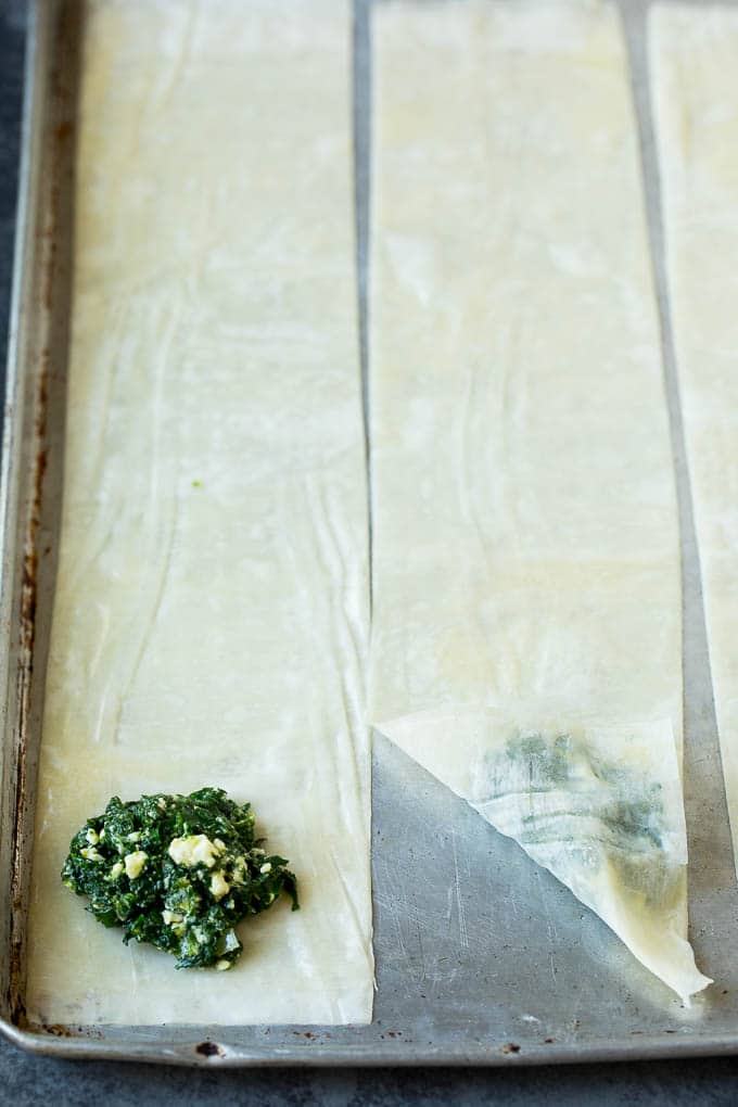 Spanakopita Recipe #appetizer #snack #spinach #cheese #edsug Strips of phyllo dough with spoonfuls of filling on top.