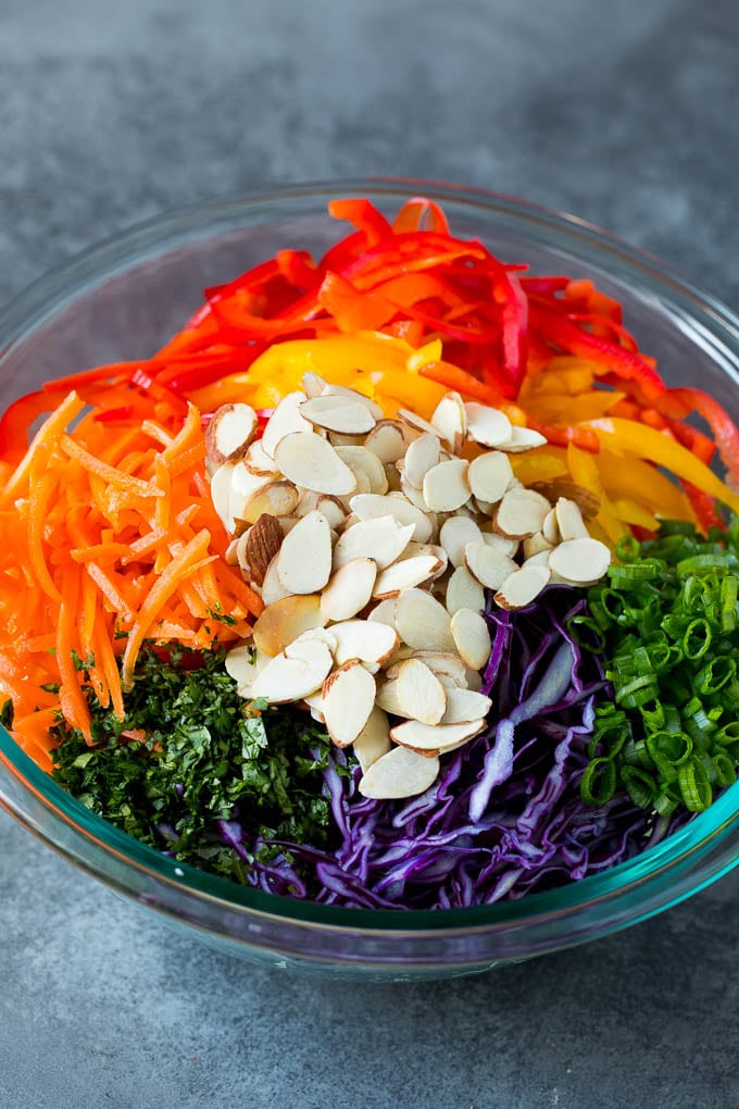 Asian Slaw Recipe #salad #slaw #sidedish #edsug Shredded cabbage, vegetables and almonds in a bowl.
