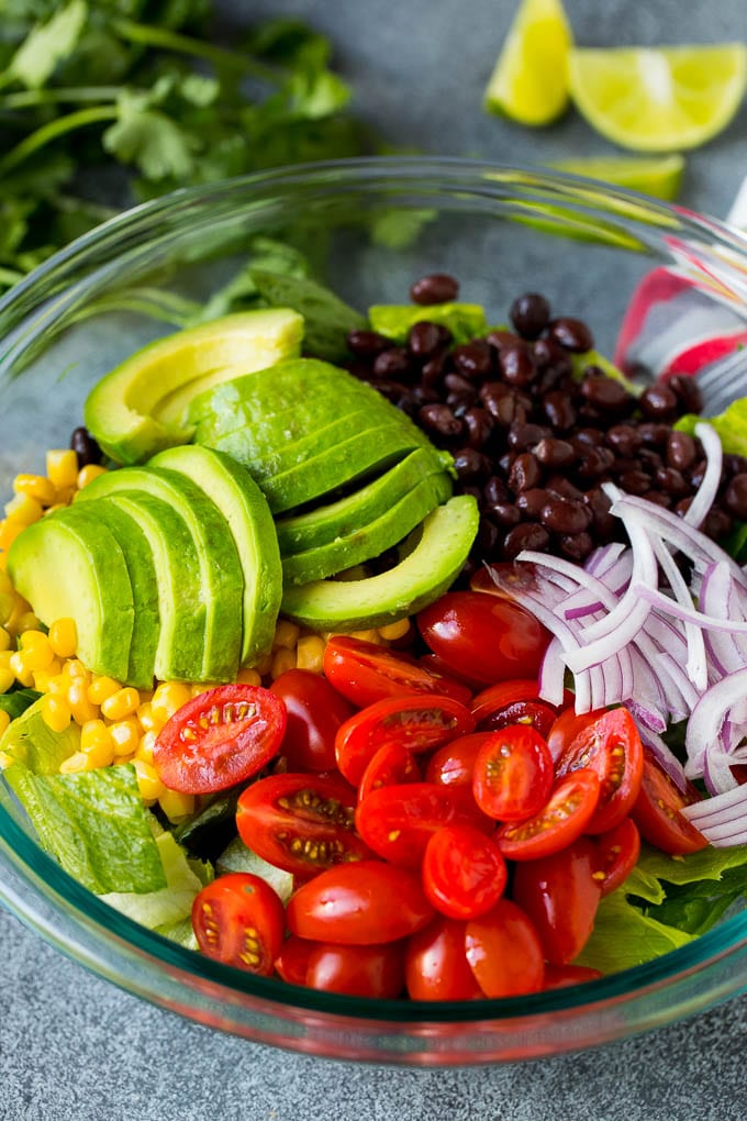 Mexican Salad Recipe #salad #corn #beans #avocado #tomatoes #edsug Lettuce, tomatoes, onion, corn, avocado and black beans in a bowl.