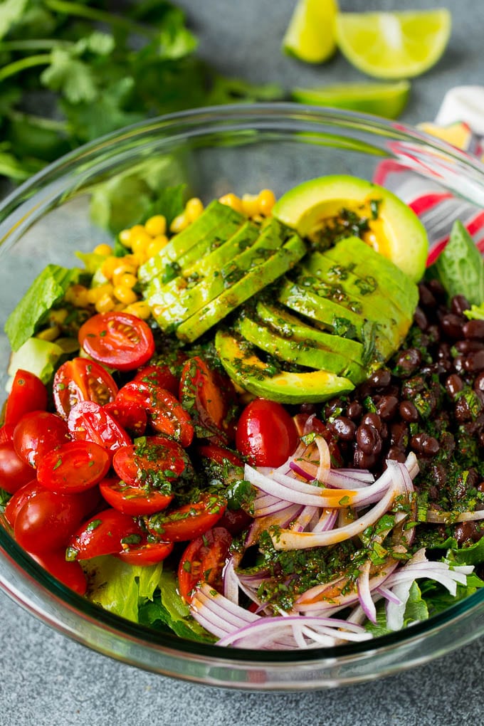 Mexican Salad Recipe #salad #corn #beans #avocado #tomatoes #edsug Dressing poured over a bowl of lettuce, tomatoes, avocado and beans.