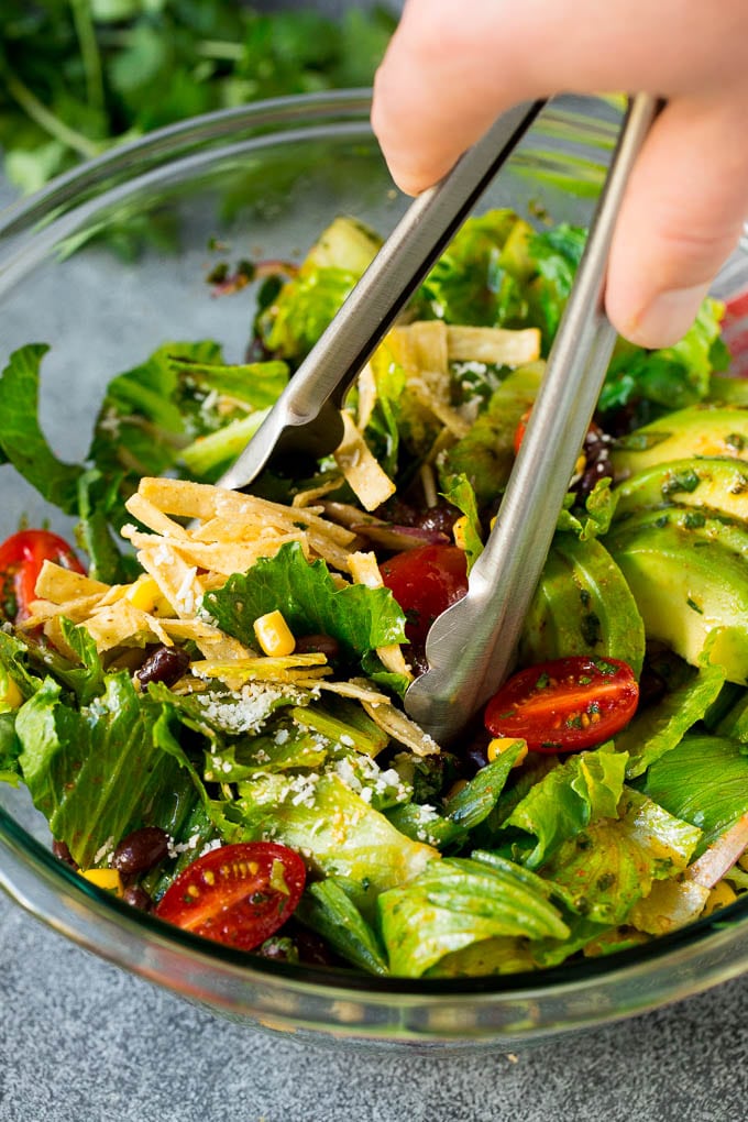 Mexican Salad Recipe #salad #corn #beans #avocado #tomatoes #edsug Tongs serving up a portion of Mexican salad.