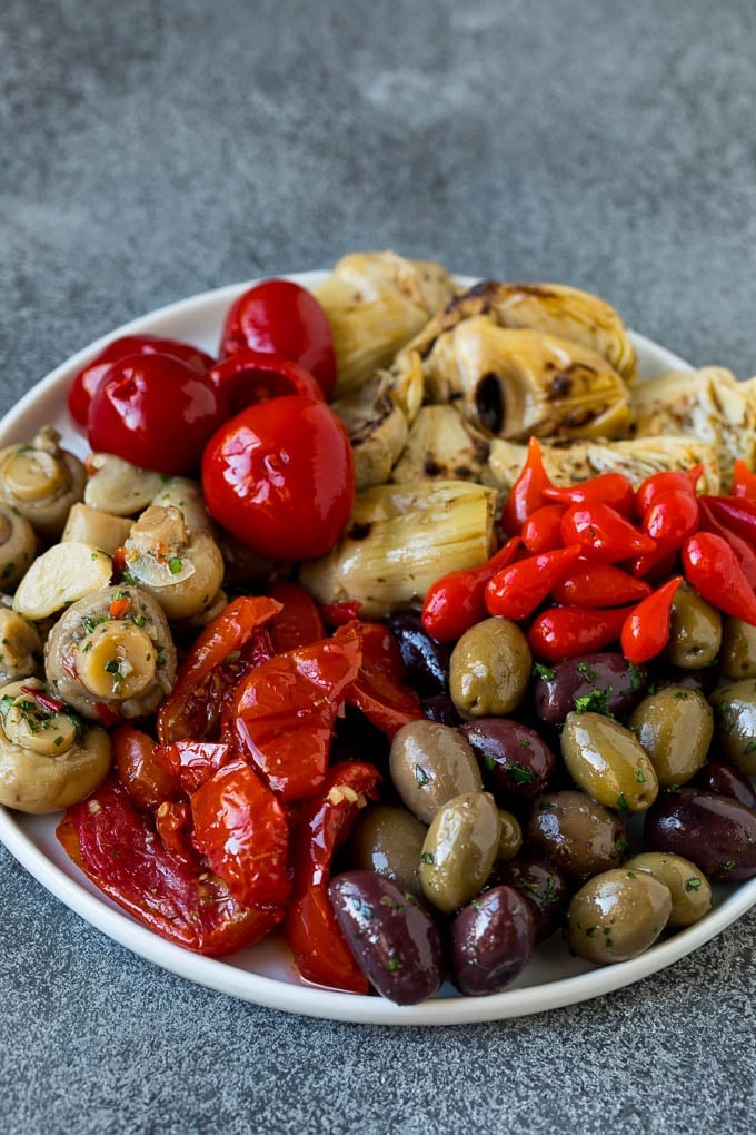 This mezze platter is filled with Mediterranean delicacies including dolmas, hummus, vegetables, pita bread and salads. #appetizer #edsug A plate of olives, peppers and grilled artichokes.