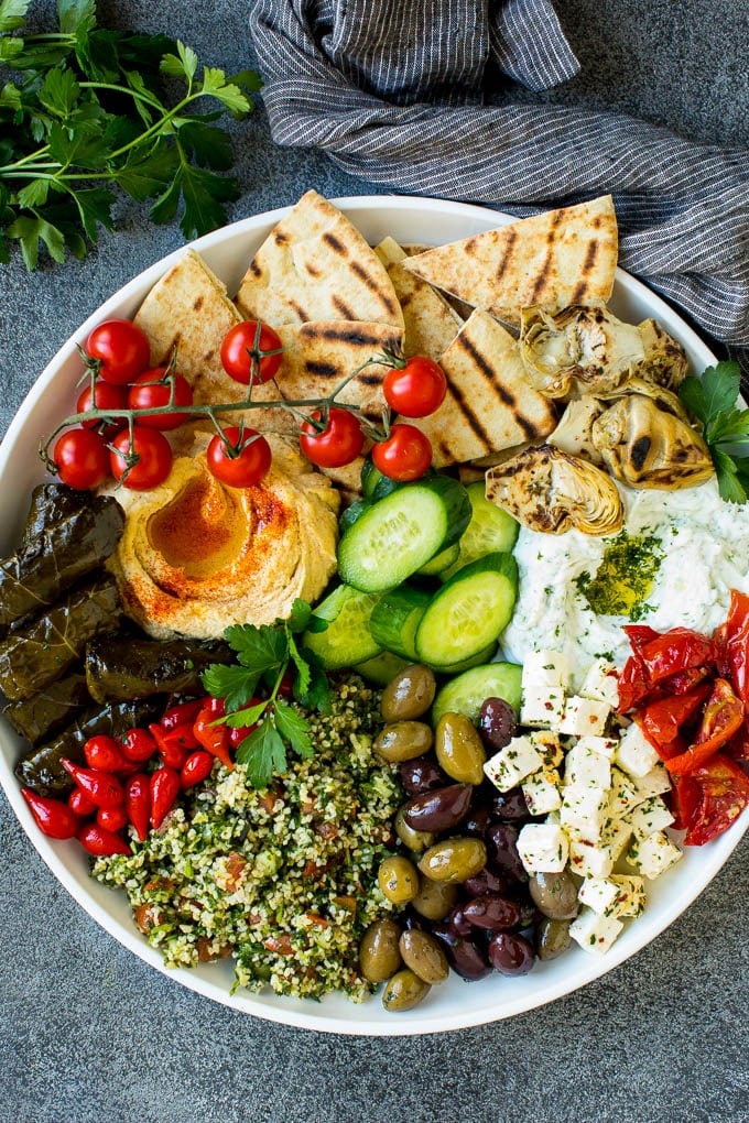 This mezze platter is filled with Mediterranean delicacies including dolmas, hummus, vegetables, pita bread and salads. #appetizer #edsug A mezze platter filled with dips, pita bread, vegetables, olives and cheese.