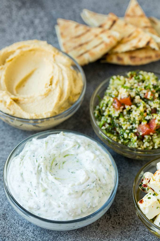 This mezze platter is filled with Mediterranean delicacies including dolmas, hummus, vegetables, pita bread and salads. #appetizer #edsug Bowls of hummus, tzatziki and tabbouleh.