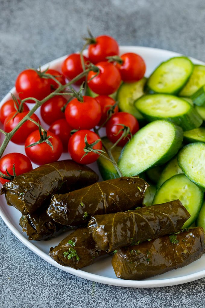 This mezze platter is filled with Mediterranean delicacies including dolmas, hummus, vegetables, pita bread and salads. #appetizer #edsug A plate of cherry tomatoes, cucumber slices and dolmas.