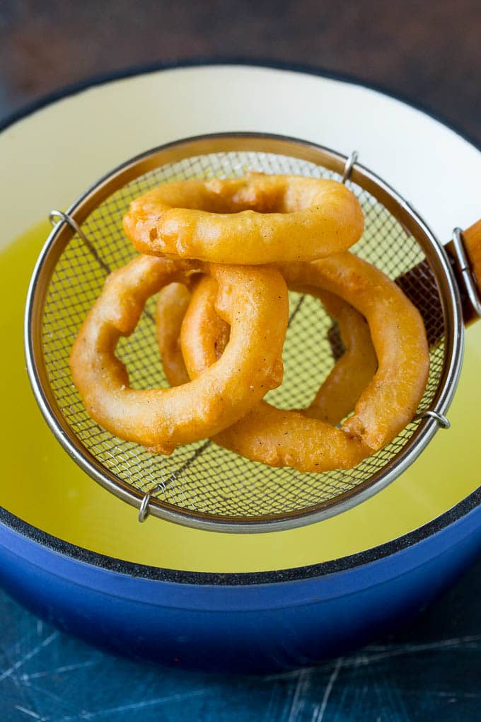 Crispy homemade onion rings that are fried in a flavorful beer batter. #onions #edsug #appetizer Fried onions coming out of a pot of oil.