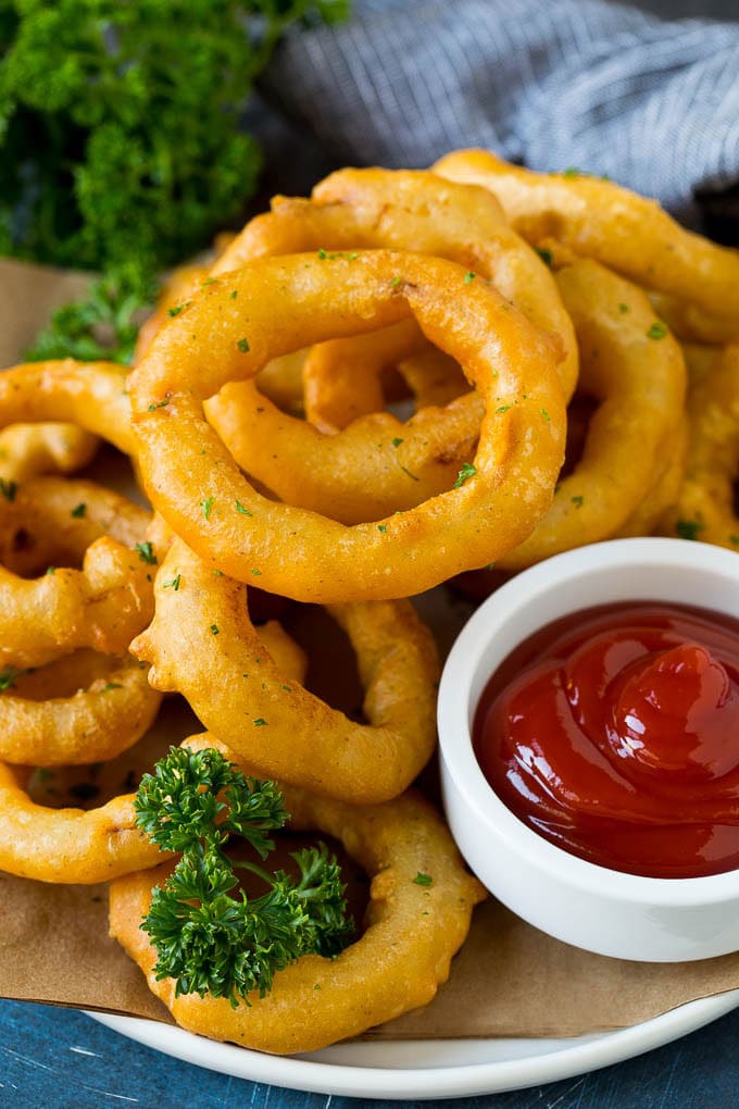 Crispy homemade onion rings that are fried in a flavorful beer batter. #onions #edsug #appetizer Fried onion rings on a plate with a side of ketchup.
