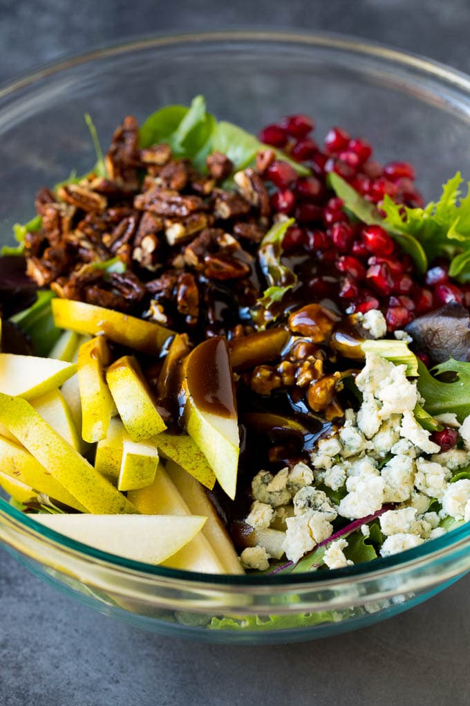 Pear Salad Recipe #salad #pears #fall #winter #dinner #edsug Balsamic dressing poured over a bowl of mixed greens, fruit and pomegranate seeds.