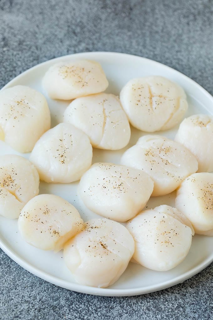 Seared scallops with a garlic and herb butter sauce. An easy and elegant dinner! #seafood #dinner #edsug Raw sea scallops on a plate.
