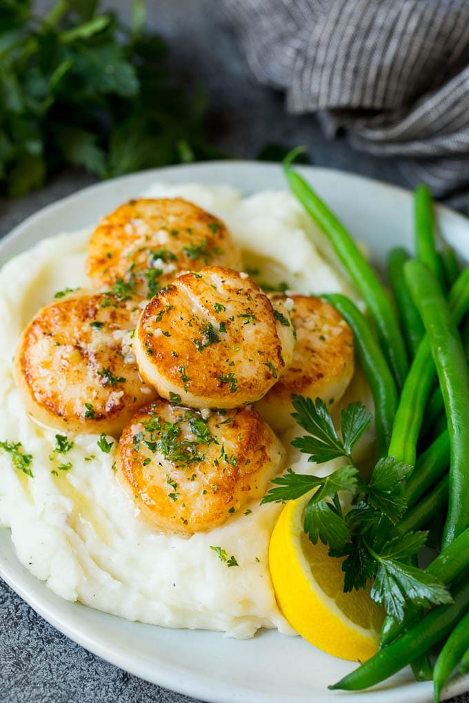 Seared scallops with a garlic and herb butter sauce. An easy and elegant dinner! #seafood #dinner #edsug Seared scallops served with mashed potatoes and green beans.