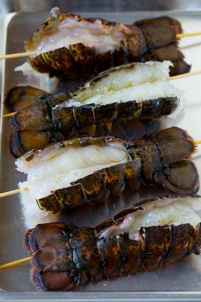 Grilled lobster tail drizzled with garlic butter is an easy and elegant dinner option. #lobster #edsug Raw lobster tails split open with skewers through them.
