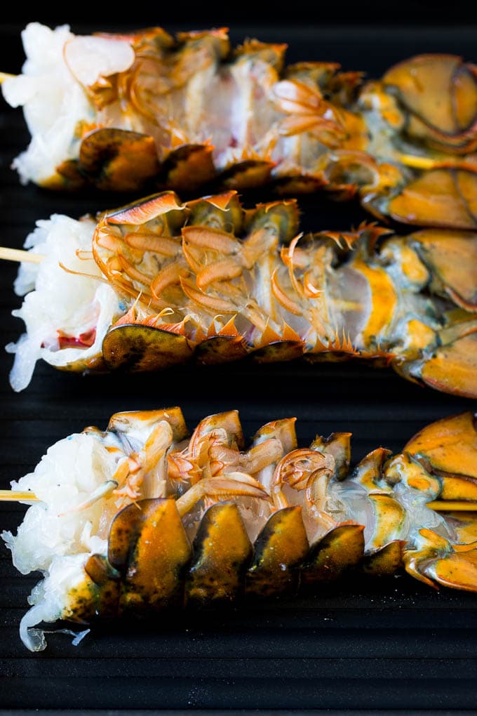 Grilled lobster tail drizzled with garlic butter is an easy and elegant dinner option. #lobster #edsug Lobster tails upside down on a grill pan.