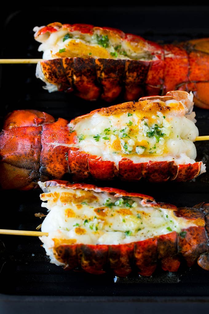 Grilled lobster tail drizzled with garlic butter is an easy and elegant dinner option. #lobster #edsug Cooked lobster tails on a grill pan, brushed with butter.
