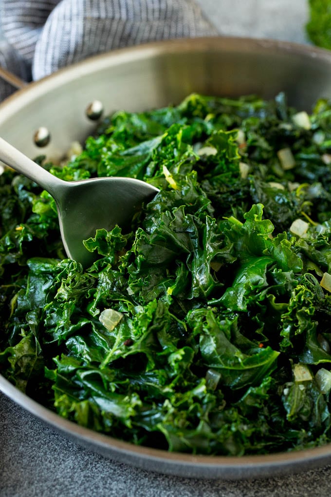 Sauteed kale flavored with olive oil and garlic, a quick and easy side dish! #kale #edsug A pan of sauteed kale with a serving spoon in it.