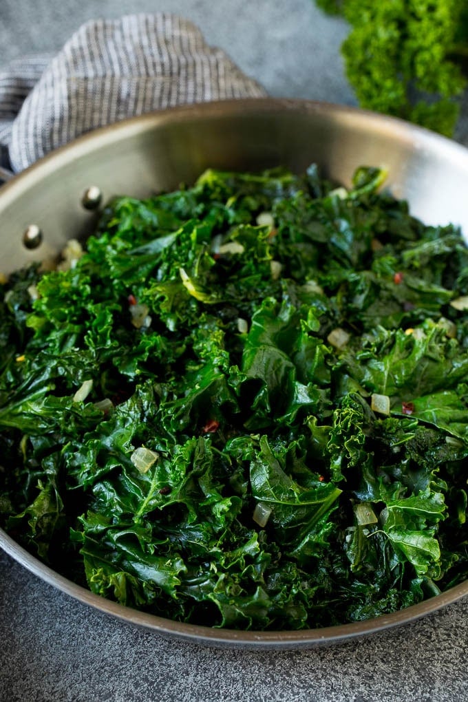 Sauteed kale flavored with olive oil and garlic, a quick and easy side dish! #kale #edsug Cooked kale with olive oil, onions and garlic.