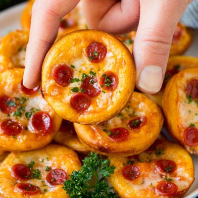 A platter of mini pizzas with a hand reaching for one.