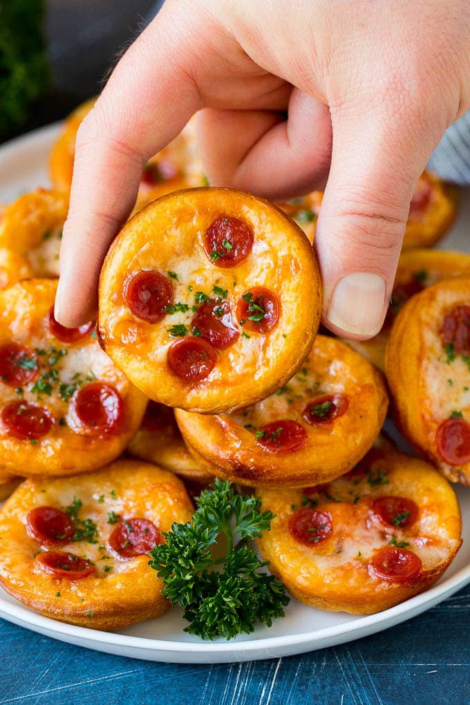 Mini pizzas topped with pepperoni are a fun and easy appetizer option. #pizza #edsug #appetizer A platter of mini pizzas with a hand reaching for one.