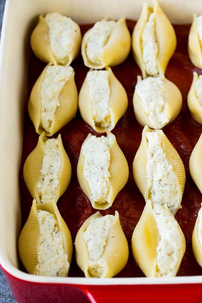 Baked stuffed shells filled with three types of cheese and topped with marinara sauce. #pasta #edsug Pasta filled with cheese on a bed of tomato sauce.