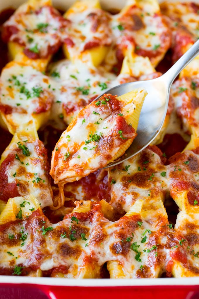 A spoon holding up stuffed shells filled with cheese and topped with marinara sauce. A serving spoon with stuffed shells filled with three types of cheese and marinara sauce.