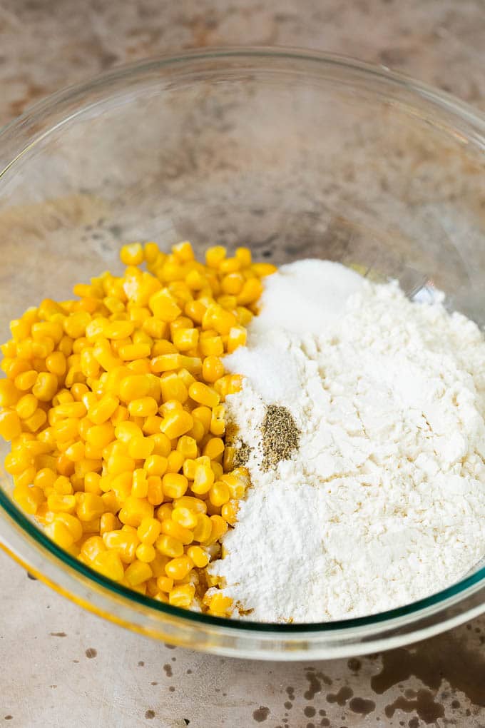 These crispy corn fritters are easy to make and are the perfect appetizer or lighter main course. #corn #edsug Flour, corn and seasonings in a mixing bowl.
