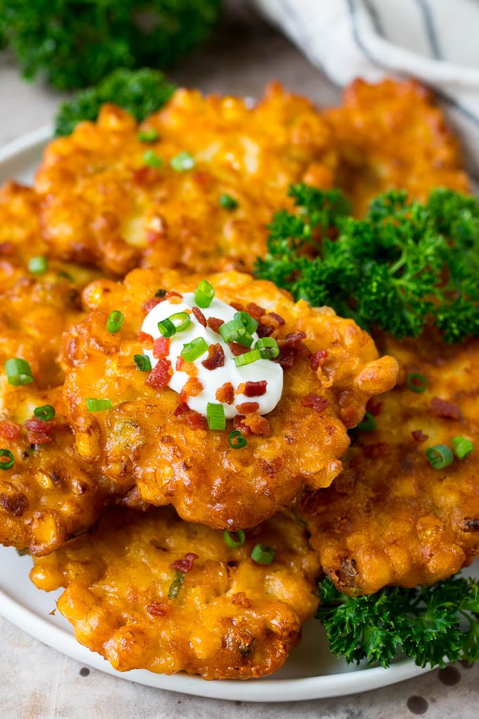 These crispy corn fritters are easy to make and are the perfect appetizer or lighter main course. #corn #edsug A plate of corn fritters garnished with parsley, and topped with sour cream.