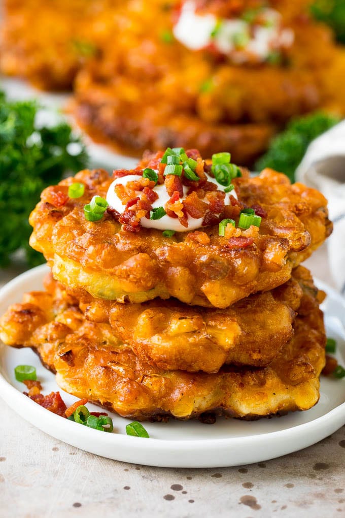These crispy corn fritters are easy to make and are the perfect appetizer or lighter main course. #corn #edsug A stack of corn fritters topped with bacon, sour cream and green onions.