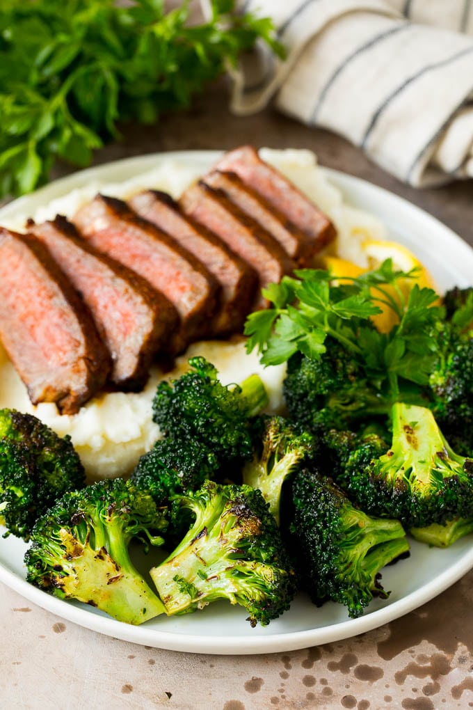 Grilled broccoli is packed with flavor and is a colorful and healthy side dish! #broccoli #edsug Grilled broccoli on a plate with steak and mashed potatoes.