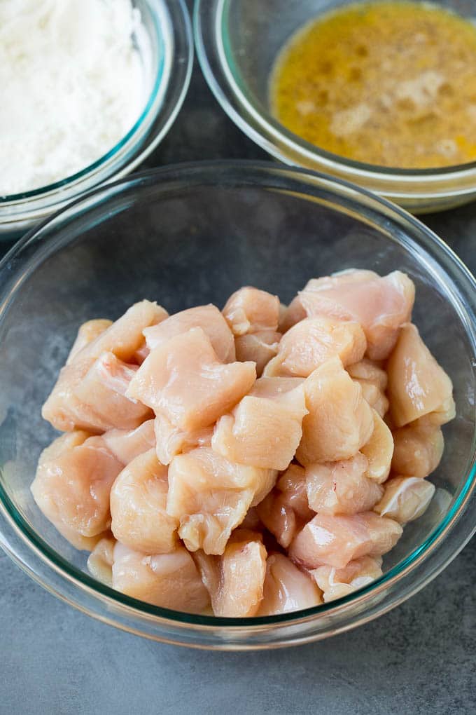 This honey chicken is crispy pieces of chicken breast that are fried to golden brown perfection, then tossed in a sweet and savory honey sauce. Bowls of diced chicken, eggs and flour.