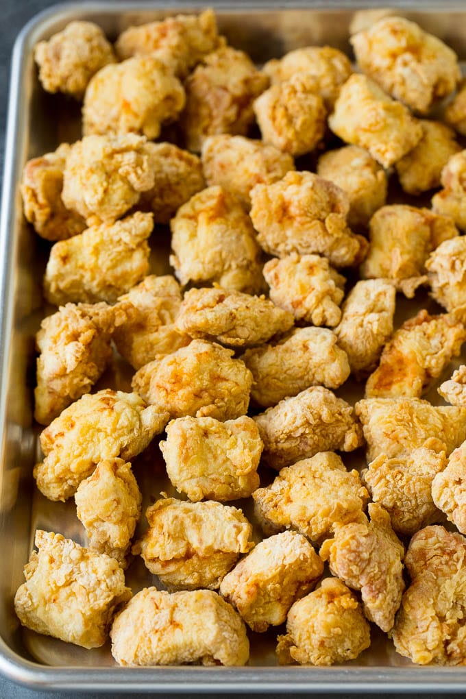 This honey chicken is crispy pieces of chicken breast that are fried to golden brown perfection, then tossed in a sweet and savory honey sauce. Deep fried chicken pieces on a sheet pan.
