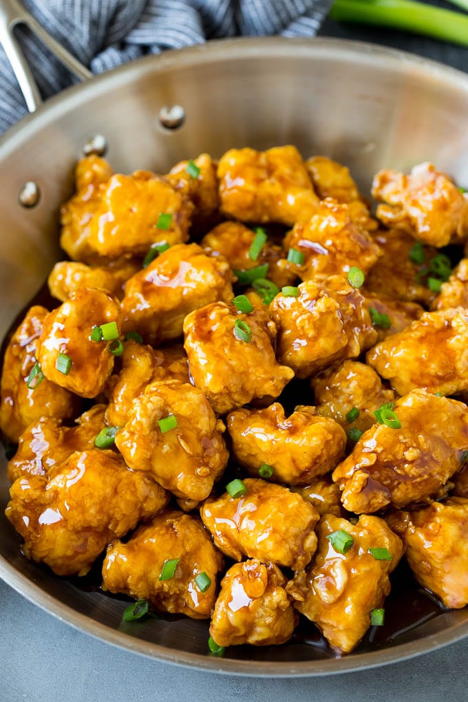 This honey chicken is crispy pieces of chicken breast that are fried to golden brown perfection, then tossed in a sweet and savory honey sauce. A pan of crispy honey chicken garnished with green onions.