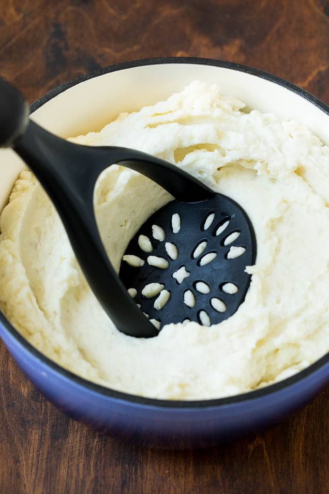 These cream cheese mashed potatoes are boiled potatoes blended with butter, milk, cream cheese and seasonings to make a rich and creamy side dish. A potato masher mashing up boiled potatoes and seasonings.