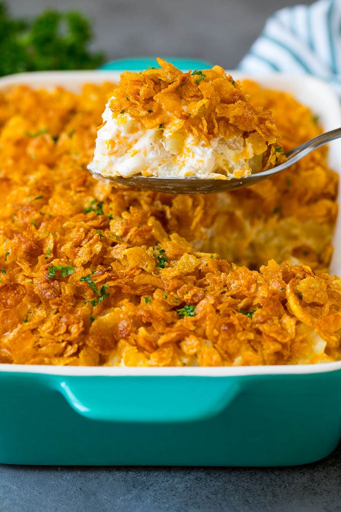 Funeral potatoes are creamy and cheesy potatoes that are topped with buttered cornflakes and baked to golden brown perfection. A spoon serving up a portion of cheesy funeral potatoes.
