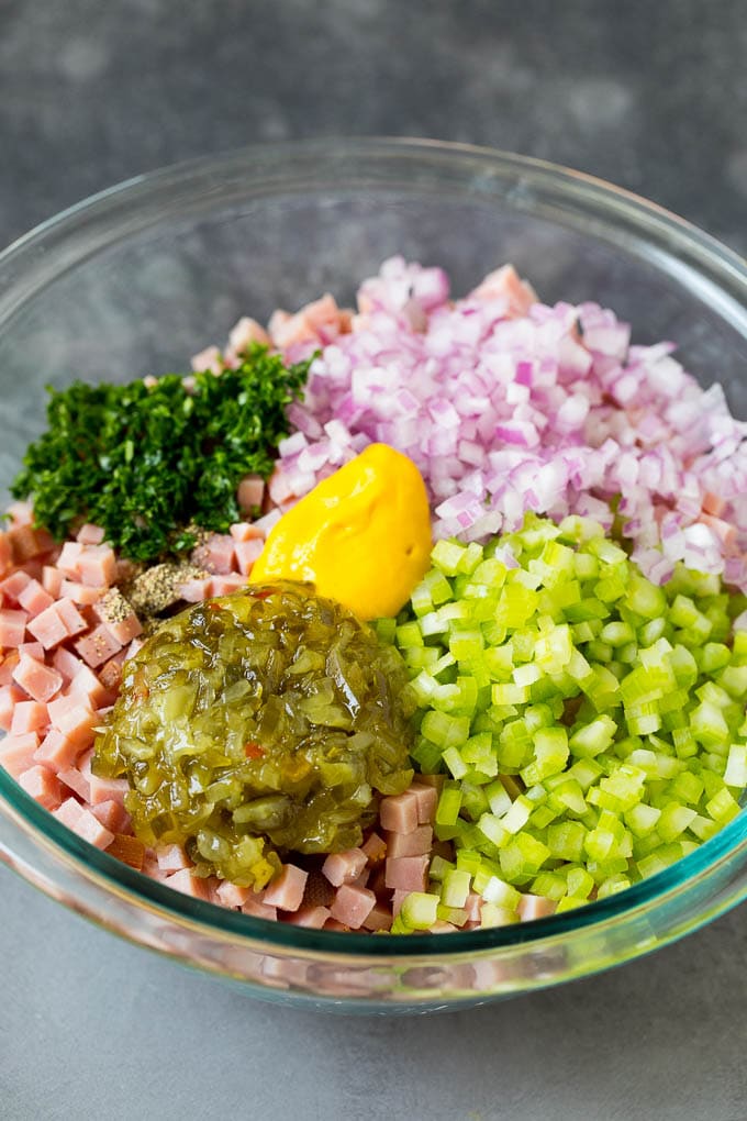 This ham salad is a blend of finely diced ham, mayonnaise, veggies and seasonings, all mixed together to form a savory and creamy salad. Finely chopped ham in a bowl with parsley, mustard, pickle relish and vegetables.