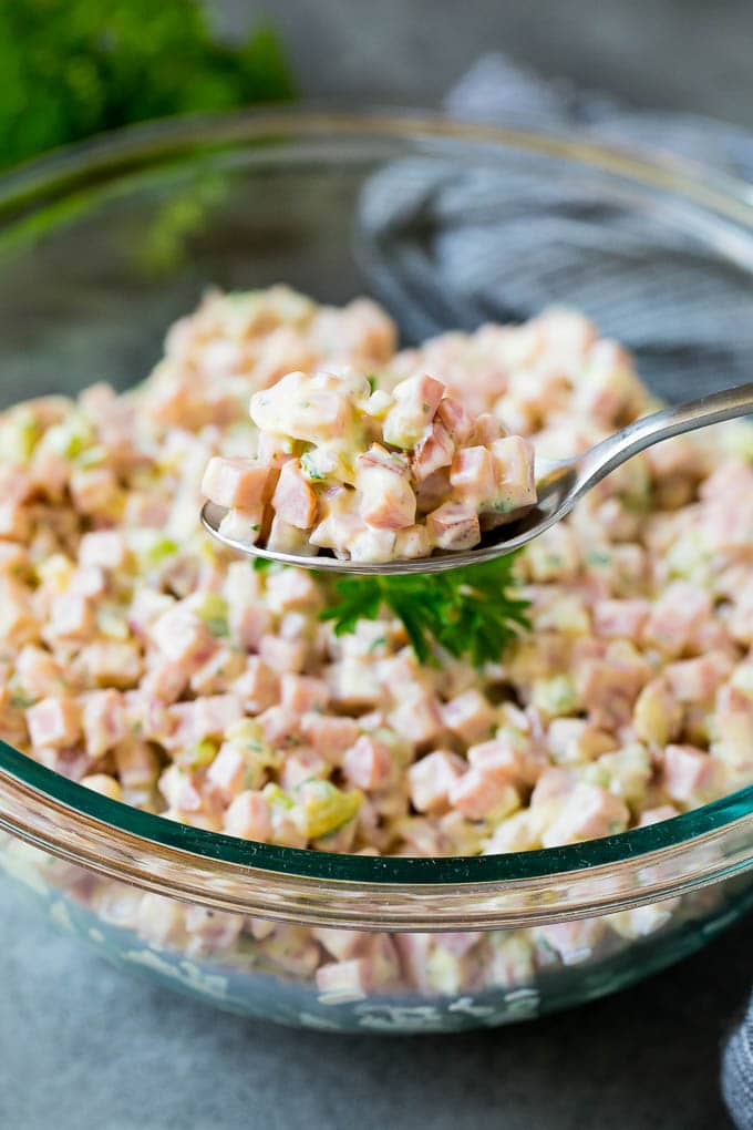 This ham salad is a blend of finely diced ham, mayonnaise, veggies and seasonings, all mixed together to form a savory and creamy salad. A spoon serving up a portion of diced ham and vegetables in a creamy dressing.