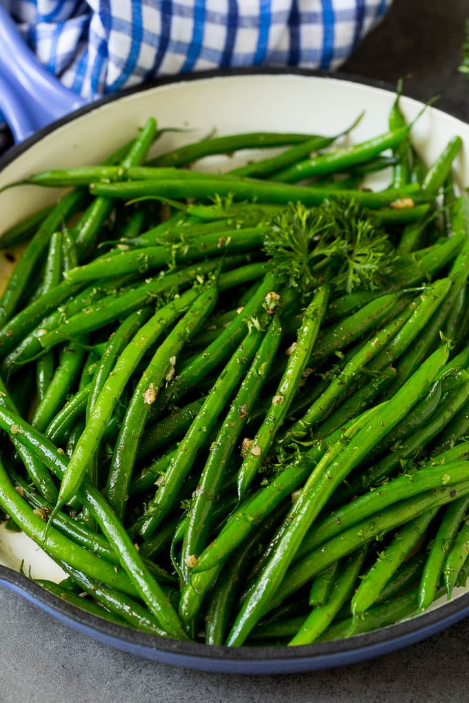 These sauteed green beans are cooked in butter, garlic and an assortment of fresh and dried herbs. A blue skillet filled with sauteed green beans, garnished with parsley.