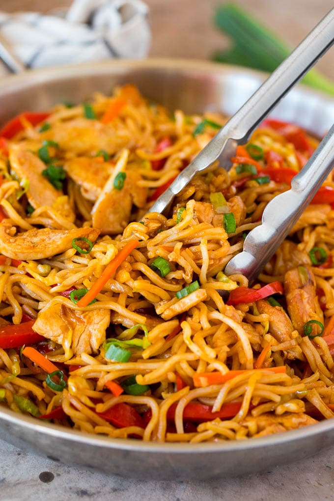 These yakisoba noodles are tender noodles stir fried with chicken and assorted vegetables in a savory sauce. Tongs serving up a portion of yakisoba noodles with vegetables and chicken.