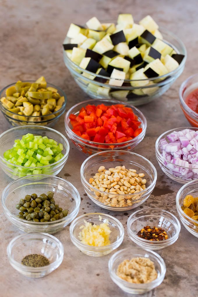 This caponata recipe is a sweet and savory blend of eggplant, peppers, tomatoes and olives, all simmered together to create a delicious appetizer. Bowls of ingredients including diced vegetables, olives, raisins and seasonings.