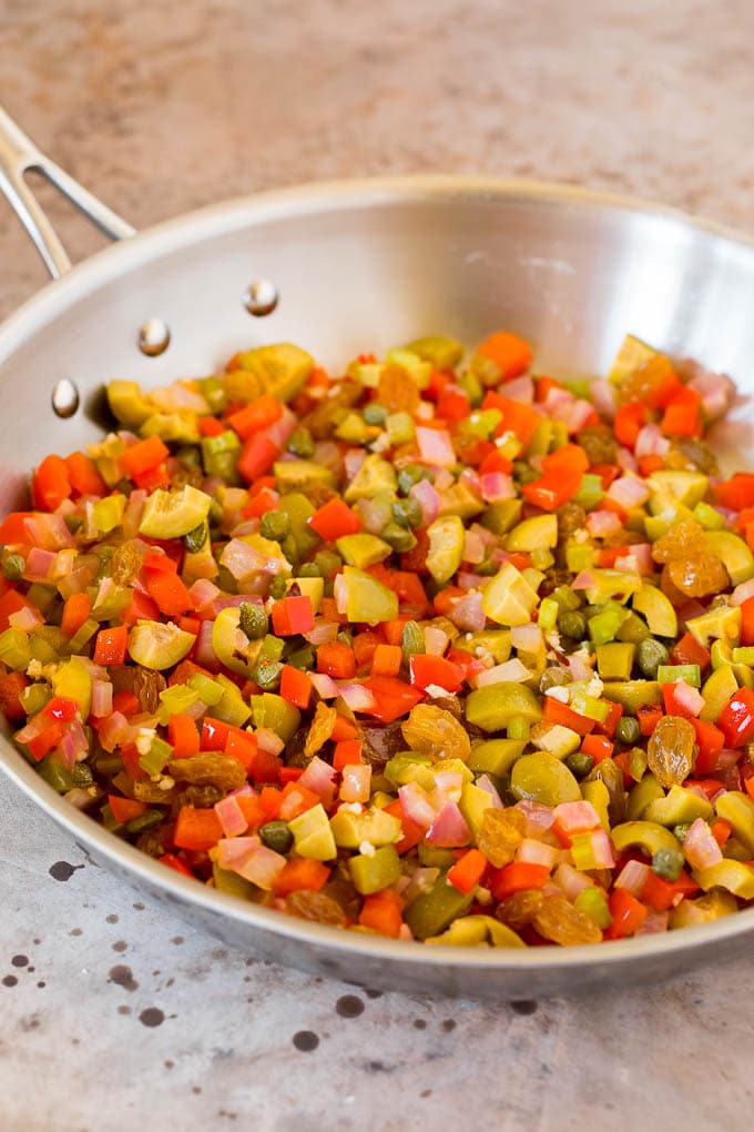 This caponata recipe is a sweet and savory blend of eggplant, peppers, tomatoes and olives, all simmered together to create a delicious appetizer. Olives, vegetables and capers in a skillet.