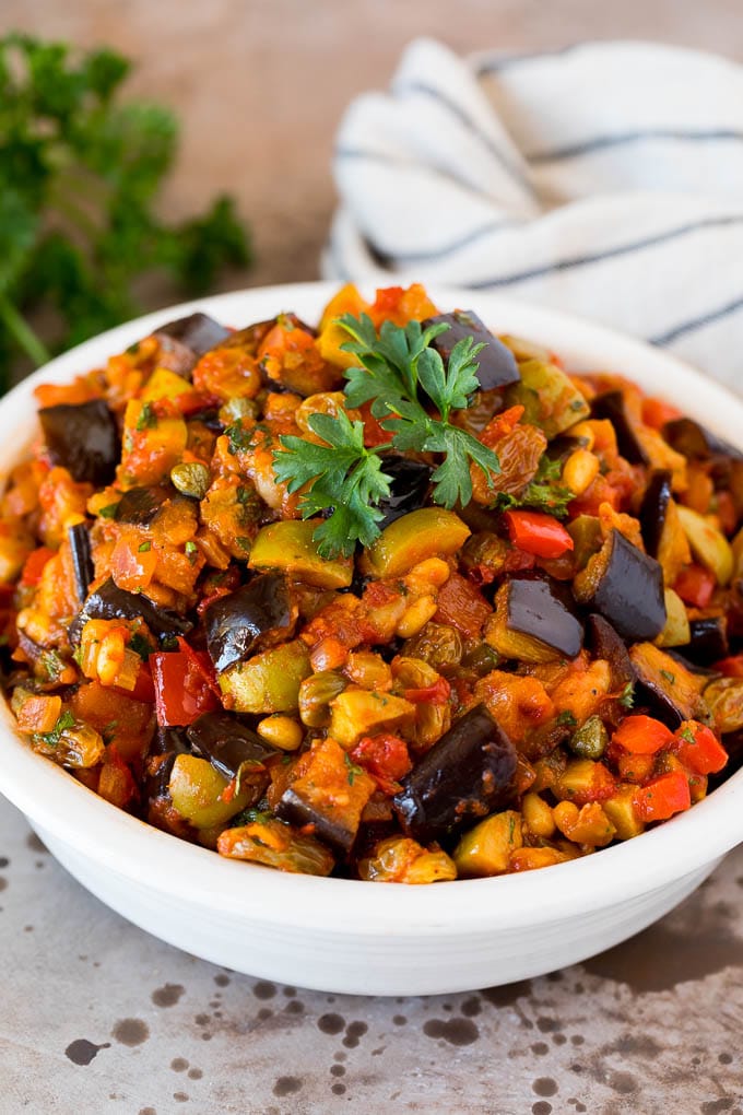 This caponata recipe is a sweet and savory blend of eggplant, peppers, tomatoes and olives, all simmered together to create a delicious appetizer. A serving bowl of caponata topped with fresh parsley.