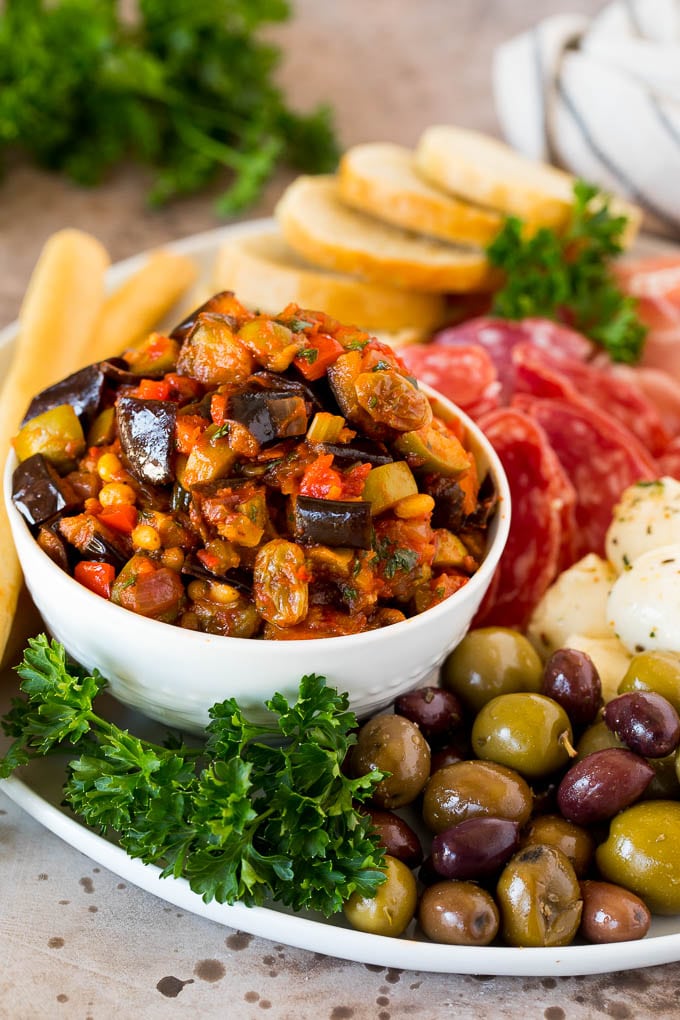 This caponata recipe is a sweet and savory blend of eggplant, peppers, tomatoes and olives, all simmered together to create a delicious appetizer. A bowl of eggplant caponata served with olives, cured meats and bread.