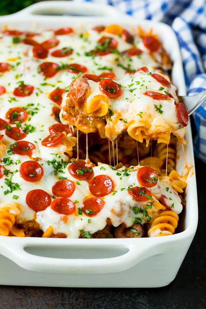 This pizza casserole is pasta simmered in tomato sauce with pepperoni, sausage, olives and bell peppers. A spoon serving up a portion of pizza casserole.
