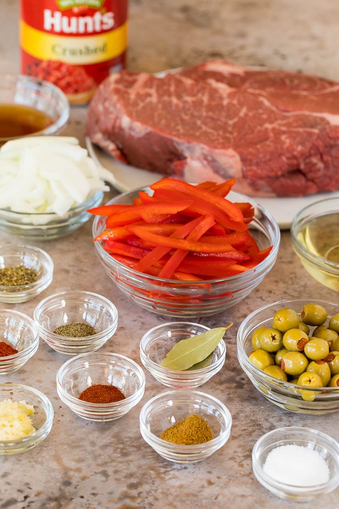 This ropa vieja recipe is a traditional dish of beef roast that's simmered with tomatoes and seasonings until tender, then shredded and served with olives. Ingredients in glass bowls including onions, bell pepper, olives and seasonings.