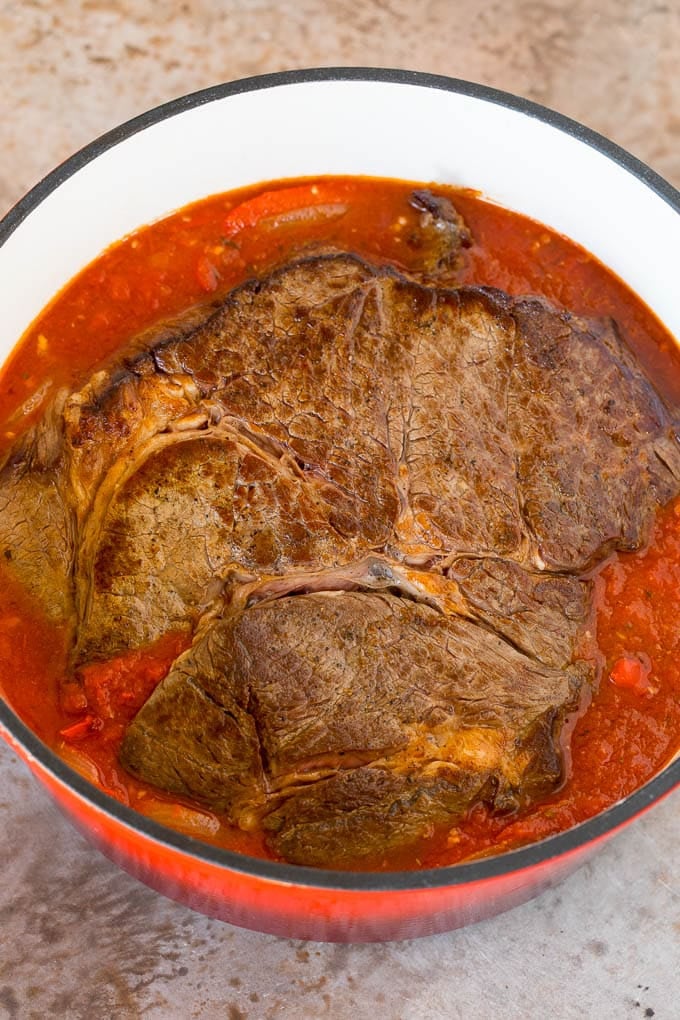 This ropa vieja recipe is a traditional dish of beef roast that's simmered with tomatoes and seasonings until tender, then shredded and served with olives. A seared roast in a pot of tomato and pepper sauce.