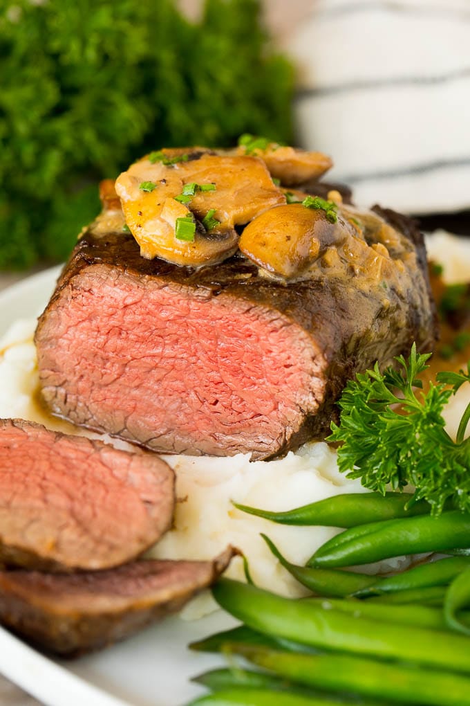 This Steak Diane recipe is beef tenderloin medallions that are seared and coated in a savory mushroom sauce. Sliced Steak Diane served with mashed potatoes and green beans.