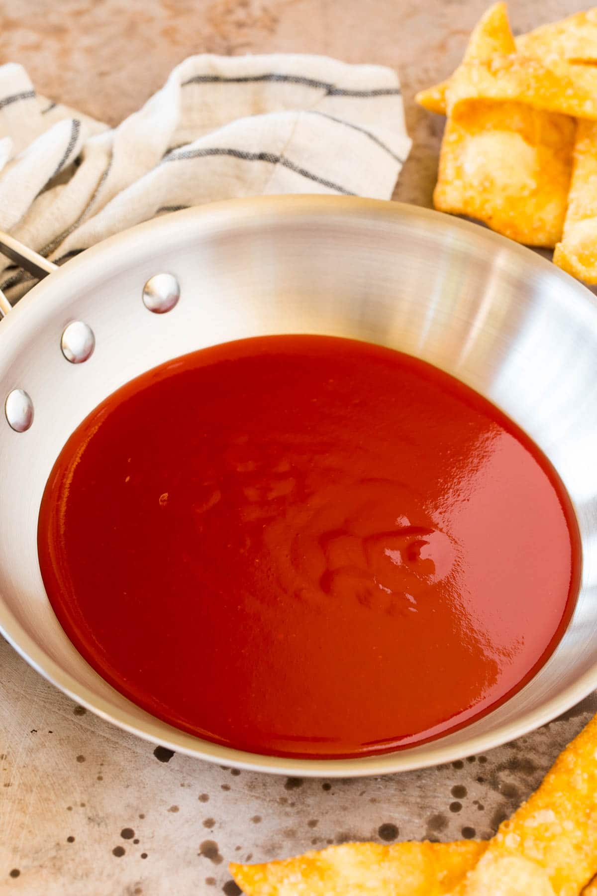 This sweet and sour sauce is a homemade version of the classic Asian sauce that takes just minutes to make and uses common pantry ingredients. A pan of sauce with wontons surrounding it.